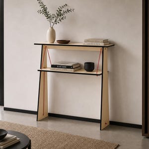 May include: A modern, two-tiered wooden console table with black trim and red accents. The table holds books, a vase with greenery, and a small bowl. The design is minimalist and the table is set against a neutral wall.