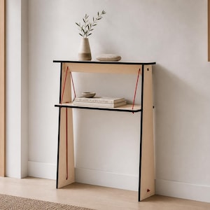 May include: A light-coloured wooden console table with black edges and thin red support cords. The table features two horizontal shelves, with the top surface holding a ceramic vase with greenery and a stone, and the lower shelf holding a book.