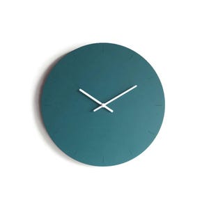 Può includere: Un orologio da parete minimalista color teal con lancette bianche. Il quadrante dell'orologio è di un colore teal uniforme con segni sottili per le ore. Le lancette sono bianche e semplici, creando un'estetica pulita e moderna.