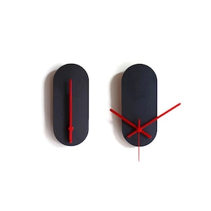 Puede incluir: Dos relojes de pared minimalistas. Cada reloj tiene una esfera ovalada alargada de color azul marino oscuro con manecillas rojas brillantes. Un reloj muestra la hora como las 12:00, el otro muestra una hora diferente.