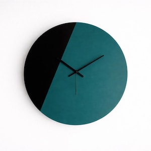 May include: A modern wall clock with a minimalist design. The round clock face is divided diagonally, with a black section on the left and a teal section on the right. Black clock hands indicate the time.
