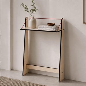 Op de afbeelding: Een moderne, minimalistische console met een lichte houten afwerking en zwarte rand. De tafel heeft een plank met een vaas, boeken en een kleine houten kom. Een rood koord accentueert de bovenkant. De tafel is ongeveer 76 cm hoog.