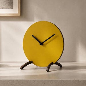 May include: A contemporary desk clock with a minimalist design. It has a bright yellow circular face, black hands, and a dark brown base. The clock is approximately 18 cm in diameter.