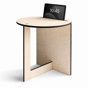 Könnte beinhalten: Ein helles Holz-Beistelltisch mit einer kreisförmigen Oberseite und einem Schlitz für ein Tablet. Das Tablet zeigt die Uhrzeit 10:45 an. Der Tisch hat ein geometrisches Design mit schwarzen Zierleisten.