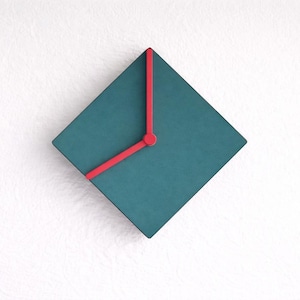May include: A teal square wall clock with red hands. The clock has a minimalist design, with the hands and the hour markers in a contrasting red color. The clock is mounted on a white wall.