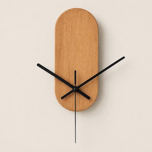 May include: A wall clock featuring a vertical, pill-shaped light brown wooden face with a visible grain texture. The clock has four thin, black metal hands of varying lengths centered on the wooden surface, indicating the time with a clean design.