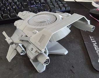May include: A light gray 3D printed model of a futuristic spacecraft featuring a large circular central turbine, angular wings, and multiple thruster ports. The structure displays visible layer lines from the printing process and has a matte finish.