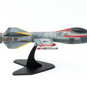 Puede incluir: Maqueta de nave espacial en tonos grises, azules y rojos, montada sobre un soporte negro. La nave espacial presenta un diseño detallado con alas, cabina y varias marcas. Es un artículo de colección.