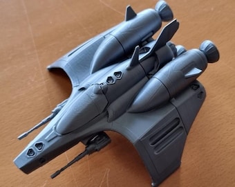 May include: A matte gray 3D printed model of a futuristic starship featuring a pointed nose, two side-mounted engines with rear thrusters, small wing fins, and two thin cannons extending from the front fuselage section of the spacecraft.