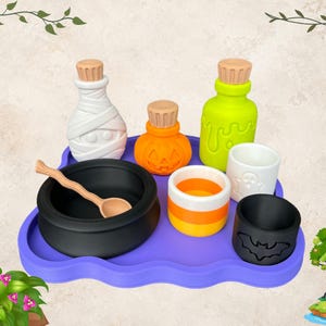 May include: A purple tray holding a black cauldron with a wooden spoon, a white mummy bottle, an orange pumpkin jar, a lime green potion bottle, a candy corn cup, a white ghost cup, and a black bat cup, all featuring Halloween-themed designs.