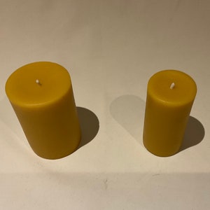 Peut inclure: Deux bougies cylindriques en cire d'abeille, l'une plus grande que l'autre, avec des m&egrave;ches blanches.
