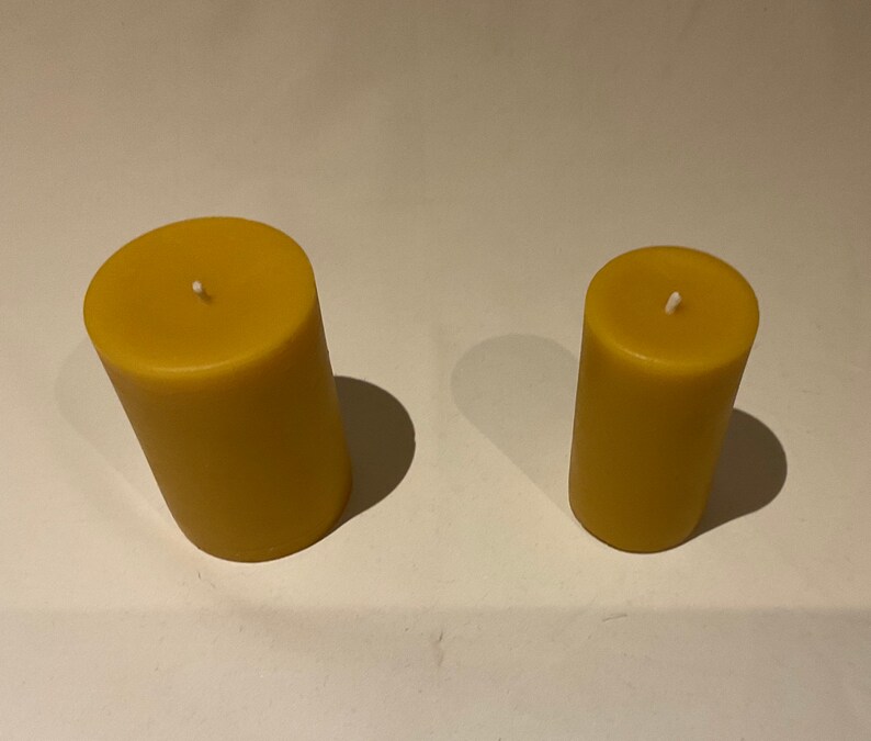 Peut inclure: Deux bougies cylindriques en cire d'abeille, l'une plus grande que l'autre, avec des m&egrave;ches blanches.