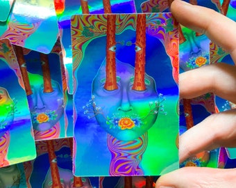 May include: Holographic art print featuring a surreal face with tree trunks for eyes and a flower in the mouth. The artwork has a vibrant color palette of blues, greens, and oranges, with a psychedelic, dreamlike quality. The print is rectangular.