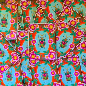 May include: A set of colorful stickers featuring a green and gold beetle with pink flowers and green leaves on a bright orange background.