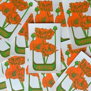 Op de afbeelding: Een verzameling witte kaarten met een oranje papaverillustratie, groene stelen en knoppen. Het woord "POPIES" is in het groen gedrukt op een olijfgroene banner. De papavers hebben gedetailleerde oranje bloemblaadjes.