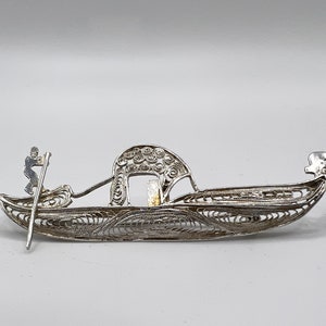 May include: A silver filigree gondola brooch featuring a figure of a gondolier holding an oar.