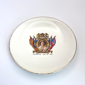 Könnte beinhalten: Ein weißer Keramikteller mit goldfarbenem Rand zeigt ein Gedenkbild von Königin Elisabeth II. Das Bild zeigt ein Porträt der Königin, das königliche Wappen und den Text "Queen Elizabeth II Coronation June 2nd 1953".