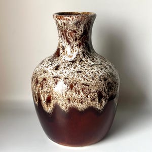 May include: A brown and white ceramic vase with a mottled glaze. The vase has a round body and a narrow neck.