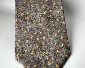 Puede incluir: Corbata estampada con un diseño repetitivo de flores amarillas y hojas verdes sobre un fondo azul claro. La corbata presenta un patrón marrón en forma de ladrillo. La corbata está hecha de tela lisa.