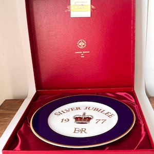 May include: A commemorative plate from the Classic Rose Collection, displayed in a red box. The plate features a white center with a crown and the words "Silver Jubilee 1977". The rim is a deep blue with a gold border.
