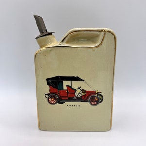 Könnte beinhalten: Eine Keramik-Karaffe in Form eines Oldtimers mit einem Metall-Ausguss. Die Karaffe ist cremefarben mit goldener Verzierung und zeigt ein rotes Oldtimer-Auto mit dem darunter gedruckten Wort "Austin".