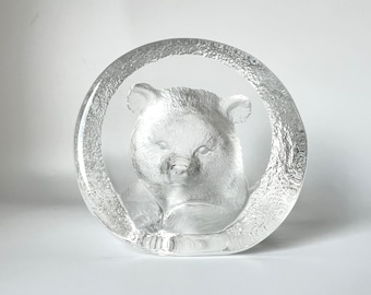May include: A clear glass sculpture of a bear's head, with the bear's face looking out from a circular frame.