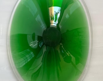 May include: A clear glass oval bowl with a vibrant green interior. The bowl has a rounded shape with a dark green sphere at the center. The glass reflects the surrounding environment, creating a unique visual effect.