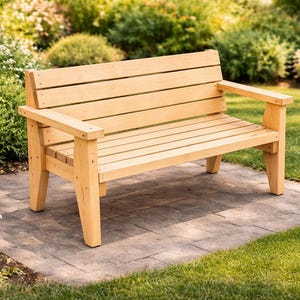 Può includere: Panca in legno chiaro con braccioli, posta su un patio in pietra. La panca ha seduta e schienale a doghe ed è circondata da erba verde e piante fiorite. La panca è lunga circa 122 cm.