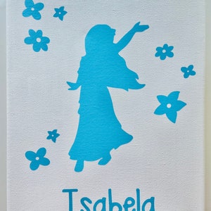 May include: A white canvas with a blue silhouette of a girl with long hair and flowers. The name "Isabella" is written in blue below the girl.