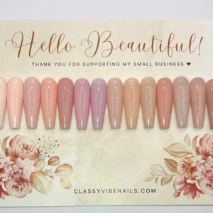 May include: A set of 15 long, almond-shaped, nude-colored press-on nails with a subtle shimmer finish. The nails are arranged in a row on a white background with floral designs and the text "Hello Beautiful! Thank you for supporting my small business." and "classyvibenails.com".