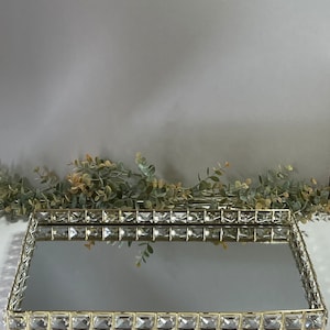 May include: A gold mirrored tray with a crystal-encrusted border. The tray is rectangular and has a reflective surface.
