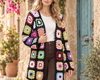 May include: A long-sleeved cardigan made of black yarn featuring a multi-colored granny square pattern. The squares are composed of various bright colors including pink, yellow, blue, orange, and white. The cardigan has an open front design.