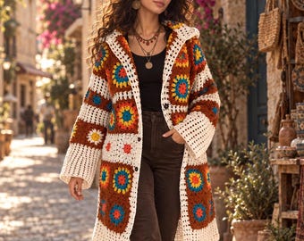 Könnte beinhalten: Eine langärmelige Häkelstrickjacke mit Granny-Square-Muster in Braun, Creme, Gelb, Blau und Rot. Das Kleidungsstück hat eine Kapuze, eine Knopfleiste vorne und eine lockere Passform, getragen über einem schwarzen Oberteil und einer dunkelbraunen Schlaghose.