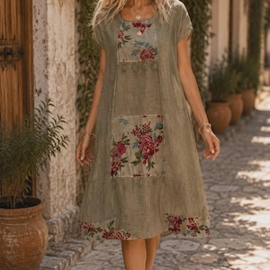 May include: A knee-length olive green dress featuring short sleeves and a round neckline. The garment is accented with rectangular panels of floral fabric in shades of red, blue, and white, positioned on the chest, mid-section, and hemline.