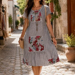 Puede incluir: Un vestido gris de manga corta con cuello redondo, dobladillo hasta la rodilla y paneles con estampado floral en el pecho, el bolsillo delantero y el borde inferior. El vestido se complementa con un collar largo y un bolso de paja tejido.