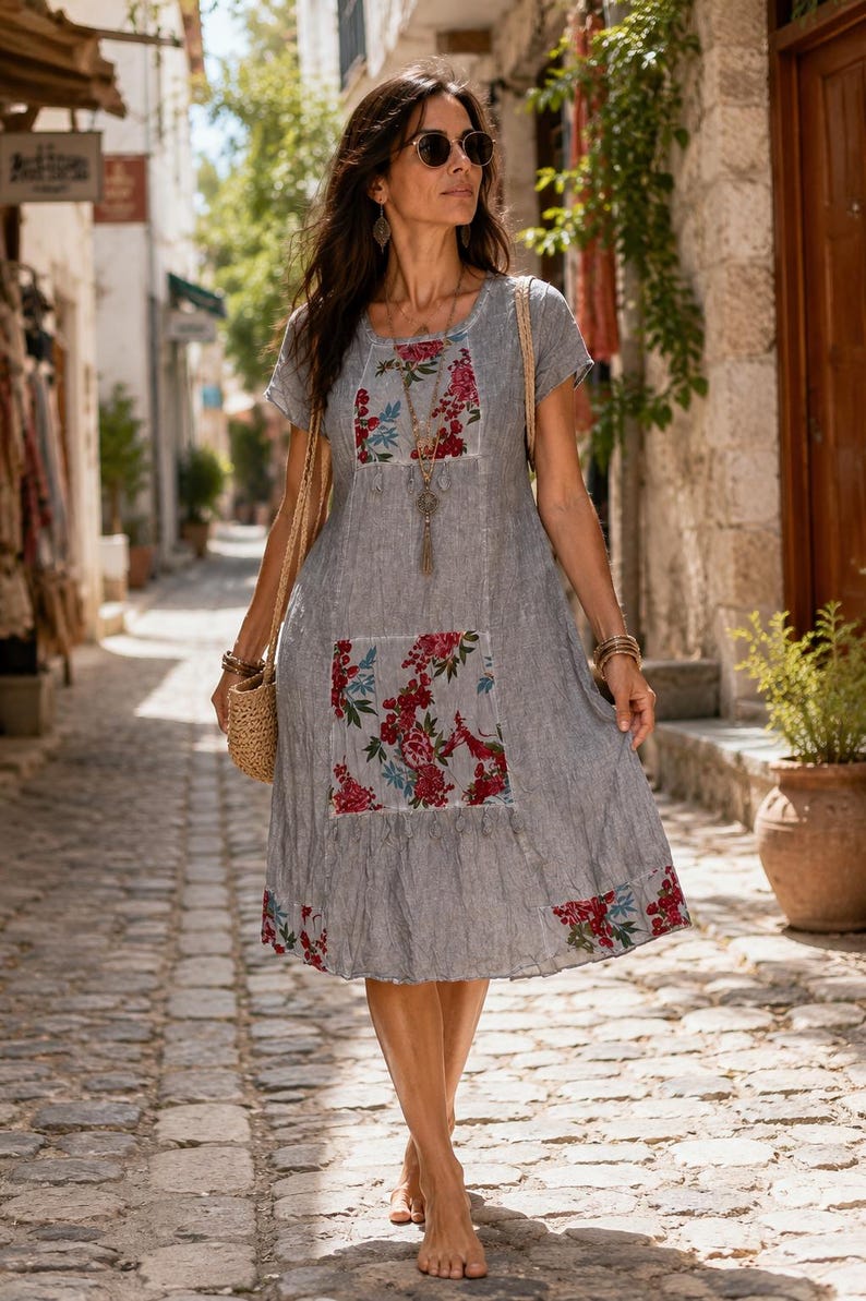 Puede incluir: Un vestido gris de manga corta con cuello redondo, dobladillo hasta la rodilla y paneles con estampado floral en el pecho, el bolsillo delantero y el borde inferior. El vestido se complementa con un collar largo y un bolso de paja tejido.