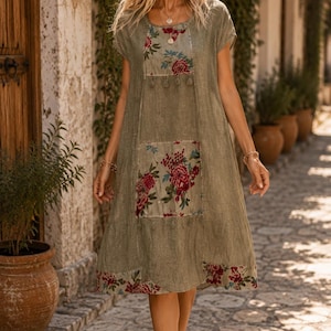 Puede incluir: Un vestido color verde oliva hasta la rodilla con mangas cortas y cuello redondo. La prenda presenta paneles rectangulares con un estampado floral en tonos rojo, blanco y azul, junto con un borde floral a juego en el dobladillo inferior.