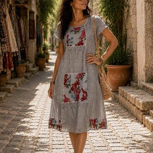 Puede incluir: Un vestido gris de manga corta con tejido texturizado y paneles florales en rojo, rosa y azul en el pecho y la parte inferior de la falda. El vestido tiene un cuello redondo y un dobladillo decorado con un patr&oacute;n floral a juego en el borde.