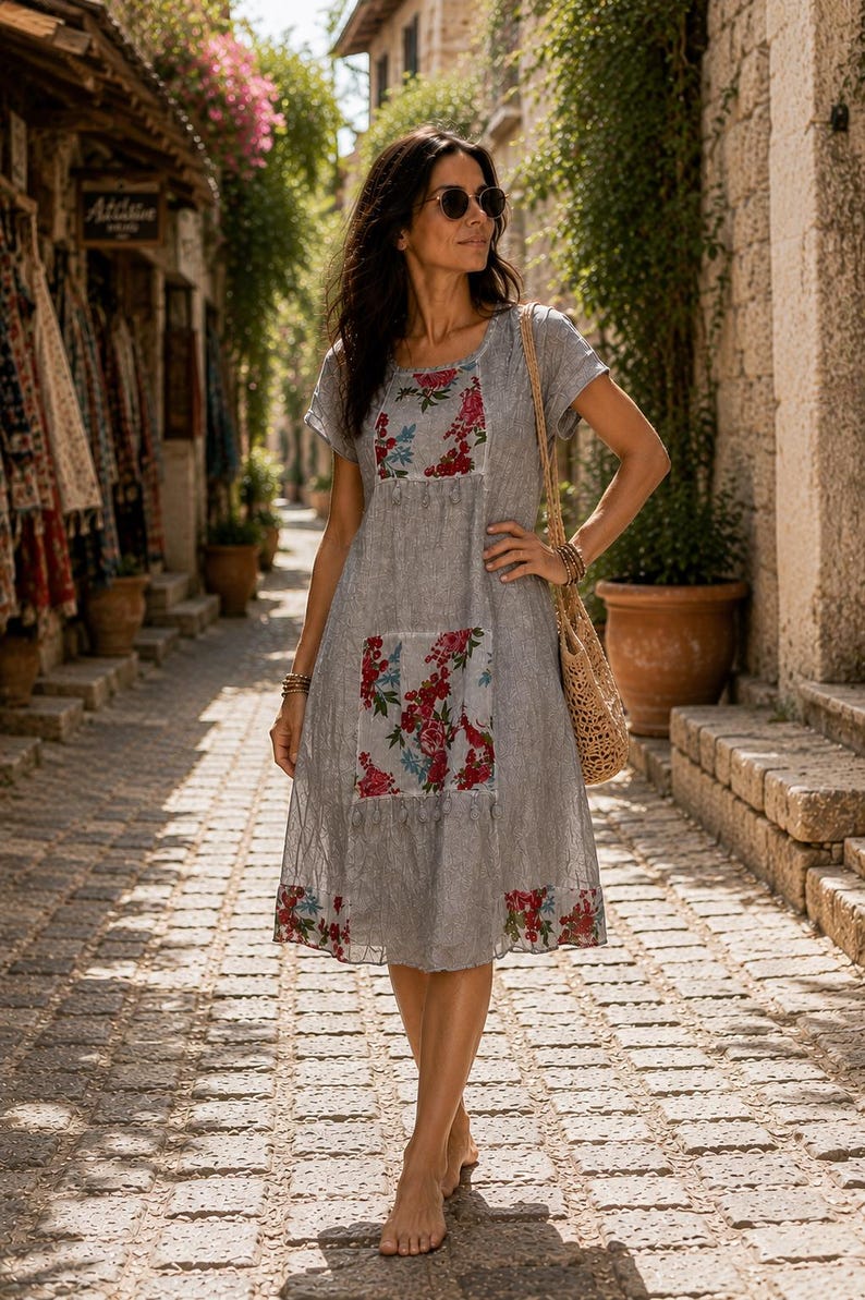 Puede incluir: Un vestido gris de manga corta con tejido texturizado y paneles florales en rojo, rosa y azul en el pecho y la parte inferior de la falda. El vestido tiene un cuello redondo y un dobladillo decorado con un patr&oacute;n floral a juego en el borde.