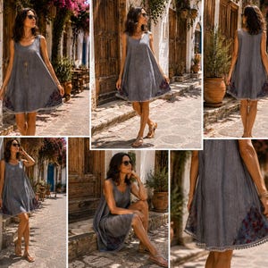 May include: A sleeveless grey A-line dress featuring a round neckline and a loose, flowing silhouette. The hem is accented with a dark floral pattern and a delicate pom-pom trim. The fabric has a subtle textured appearance throughout the garment.