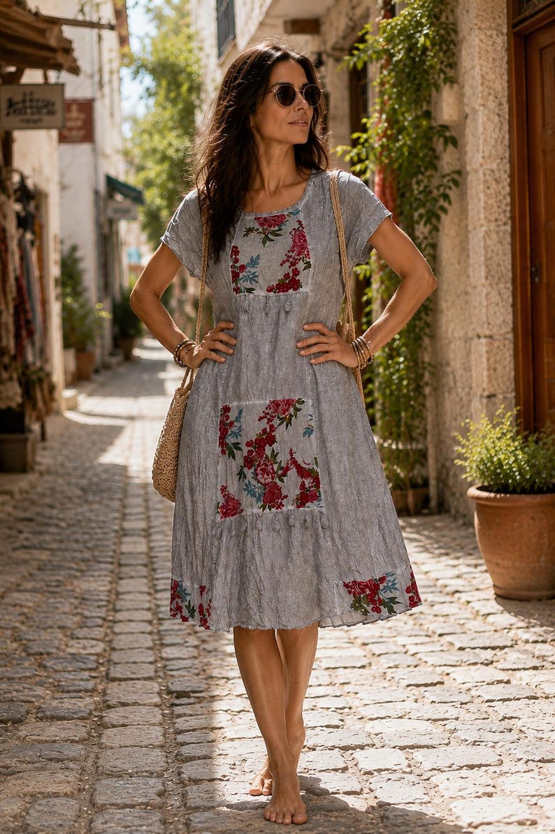 Puede incluir: Un vestido gris hasta la rodilla con mangas cortas y cuello redondo. El vestido presenta paneles rectangulares en el pecho y la falda decorados con un estampado floral en rojo, rosa y azul, rematados con peque&ntilde;as borlas grises.