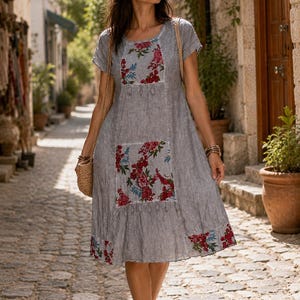 Puede incluir: Un vestido gris de manga corta en tejido texturizado con paneles florales en rojo, rosa y azul en el pecho y la falda. El vestido tiene un cuello redondo, una silueta holgada y un dobladillo decorado con un estampado floral a juego.