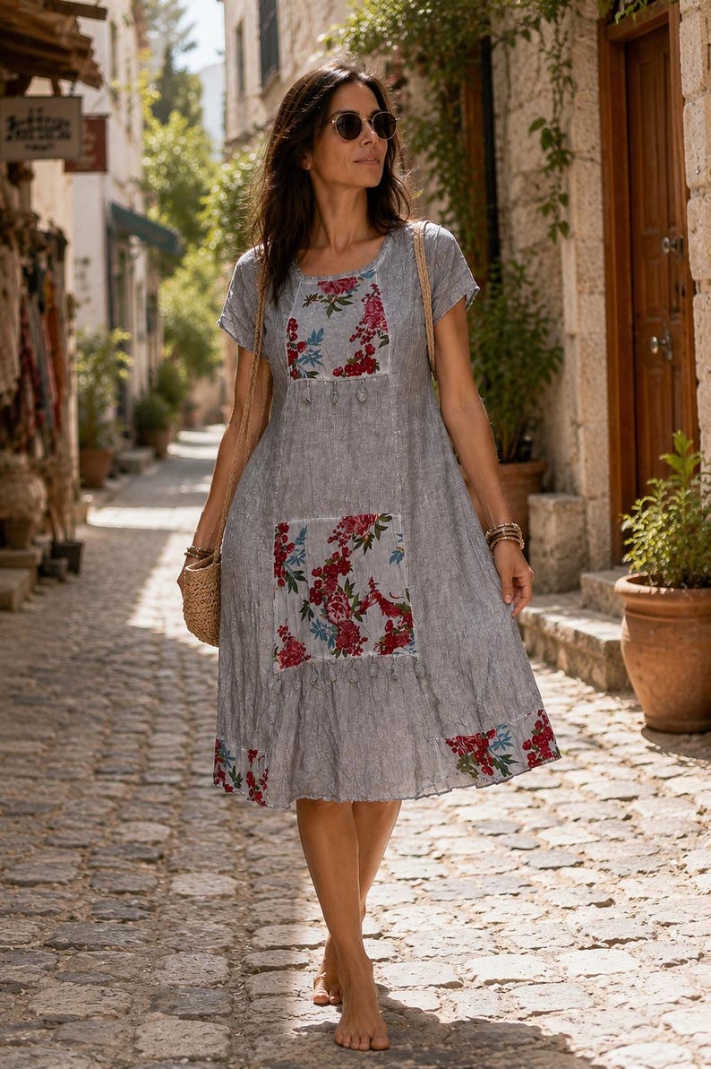 Puede incluir: Un vestido gris de manga corta en tejido texturizado con paneles florales en rojo, rosa y azul en el pecho y la falda. El vestido tiene un cuello redondo, una silueta holgada y un dobladillo decorado con un estampado floral a juego.