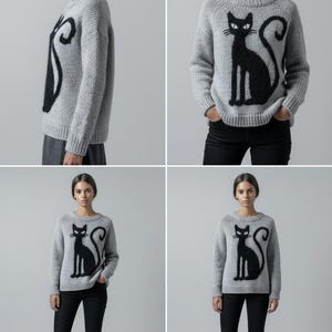 May include: A light gray sweater featuring a large black cat design. The cat is sitting upright with a curved tail. The sweater is paired with black pants and white sneakers. The model is standing in front of a gray background.