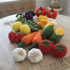 Może przedstawiać: Kolekcja szydełkowych warzyw i owoc&oacute;w, w tym czerwone jabłka, truskawki, pomidory, marchewki, kukurydza, cytryny i czosnek, ułożonych na okrągłym drewnianym stole. Ręcznie robione przedmioty są prezentowane na beżowej podkładce.