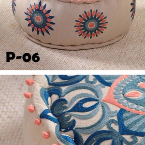 May include: A round, cream-colored ottoman with a blue and pink floral pattern. The ottoman has a pink pom-pom trim around the edge. The ottoman is labeled "P-06".