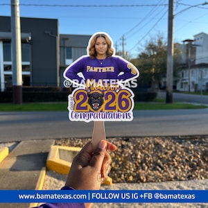 Puede incluir: Un accesorio fotográfico de graduación con una mujer con una sudadera morada de Panther. El accesorio incluye el texto "PANTHER", "@BAMATEXAS", "Class of 2026" y "Congratulations". El accesorio se sostiene con un palo de madera.
