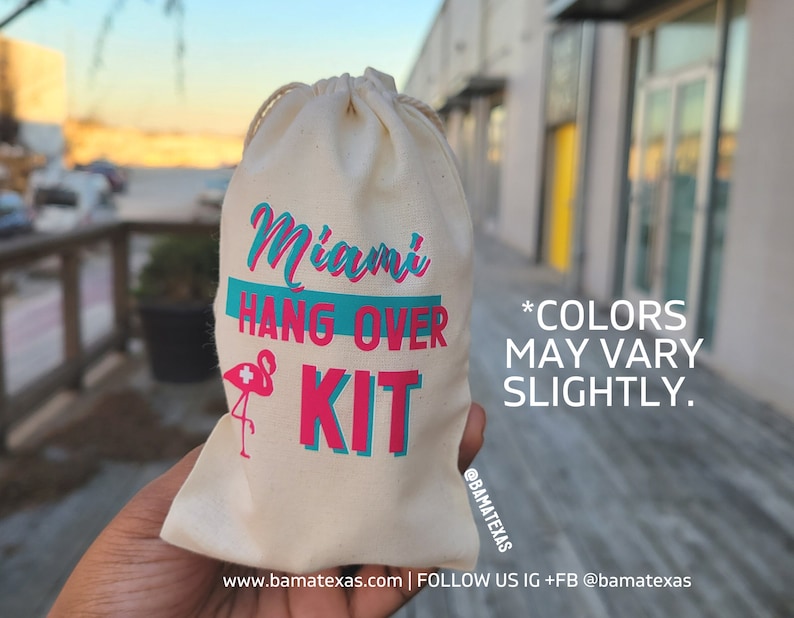 Puede incluir: Una bolsa de tela blanca con el texto "Miami Hang Over Kit" impreso en letras azules y rosas. Un flamenco rosa con una cruz blanca est&aacute; impreso en la bolsa. El texto "*COLORS MAY VARY SLIGHTLY." est&aacute; impreso debajo del nombre del kit. La bolsa est&aacute; sostenida en una mano.