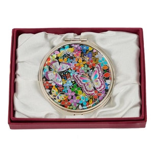 A compact mirror with a detailed, colorful butterfly and floral design, encased in a red box with a satin-like fabric lining