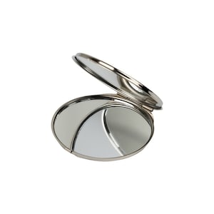 This is an image showing an open, round compact mirror at an angle, which allows us to see the reflective surface inside. It appears to have a metallic finish and is photographed agai